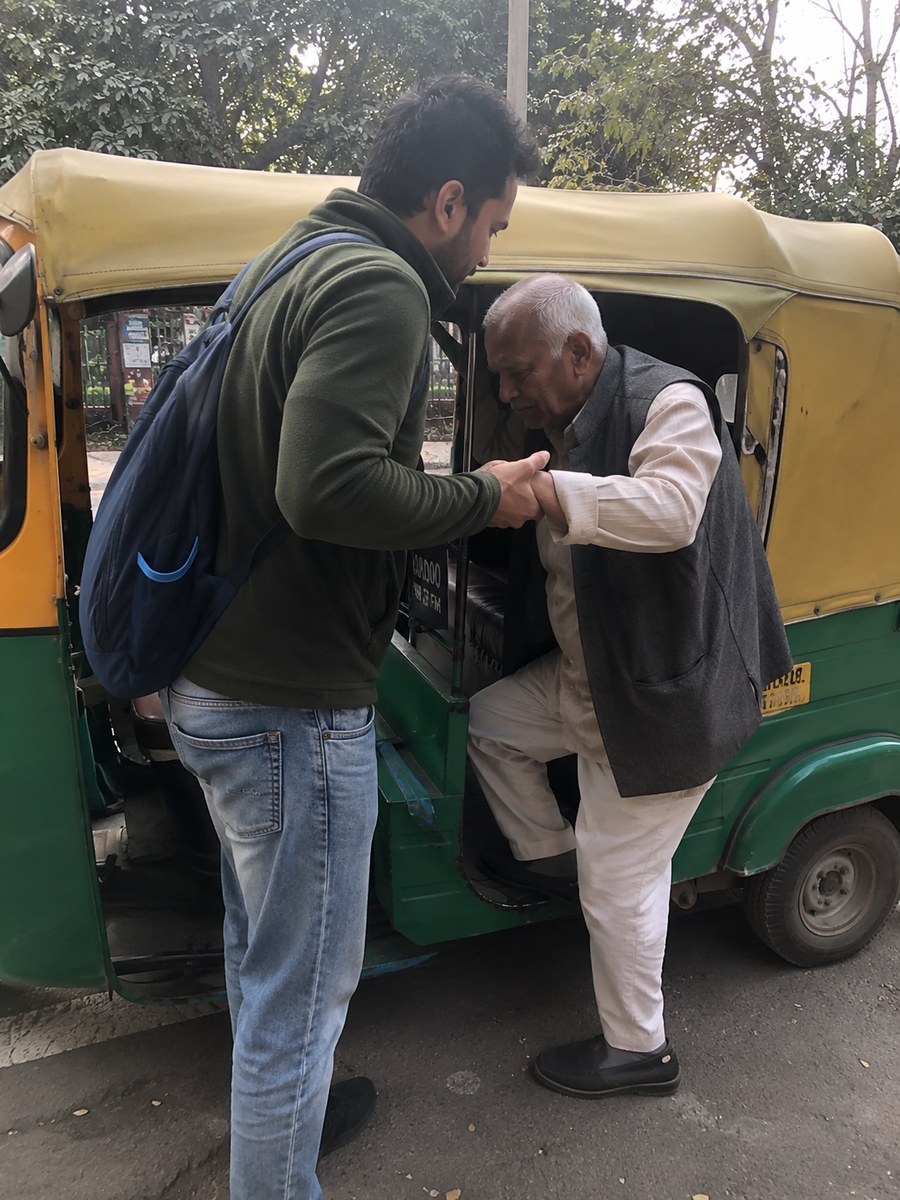 Companion helping an elderly man into an auto-rickshaw